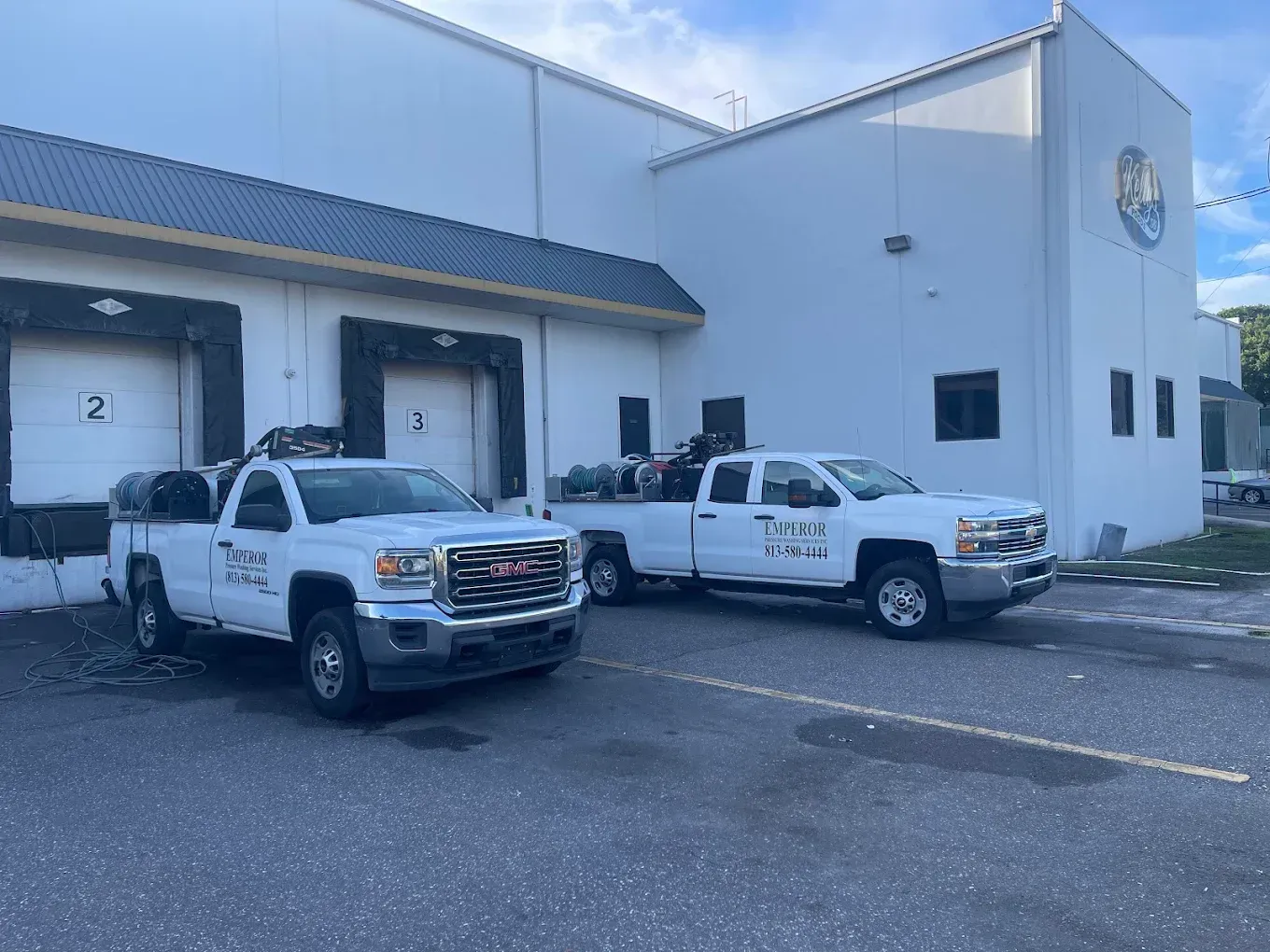 Two white pickup trucks parked outside a gray industrial building with loading docks.