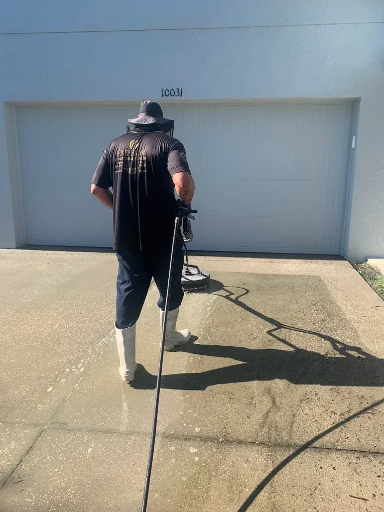 Person pressure-washing a driveway in front of a closed garage on a sunny day