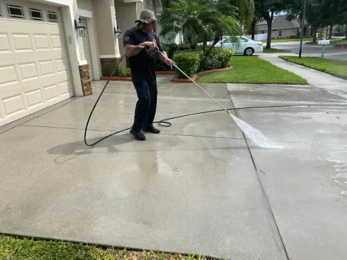 Person pressure washing a concrete driveway outside a suburban home.