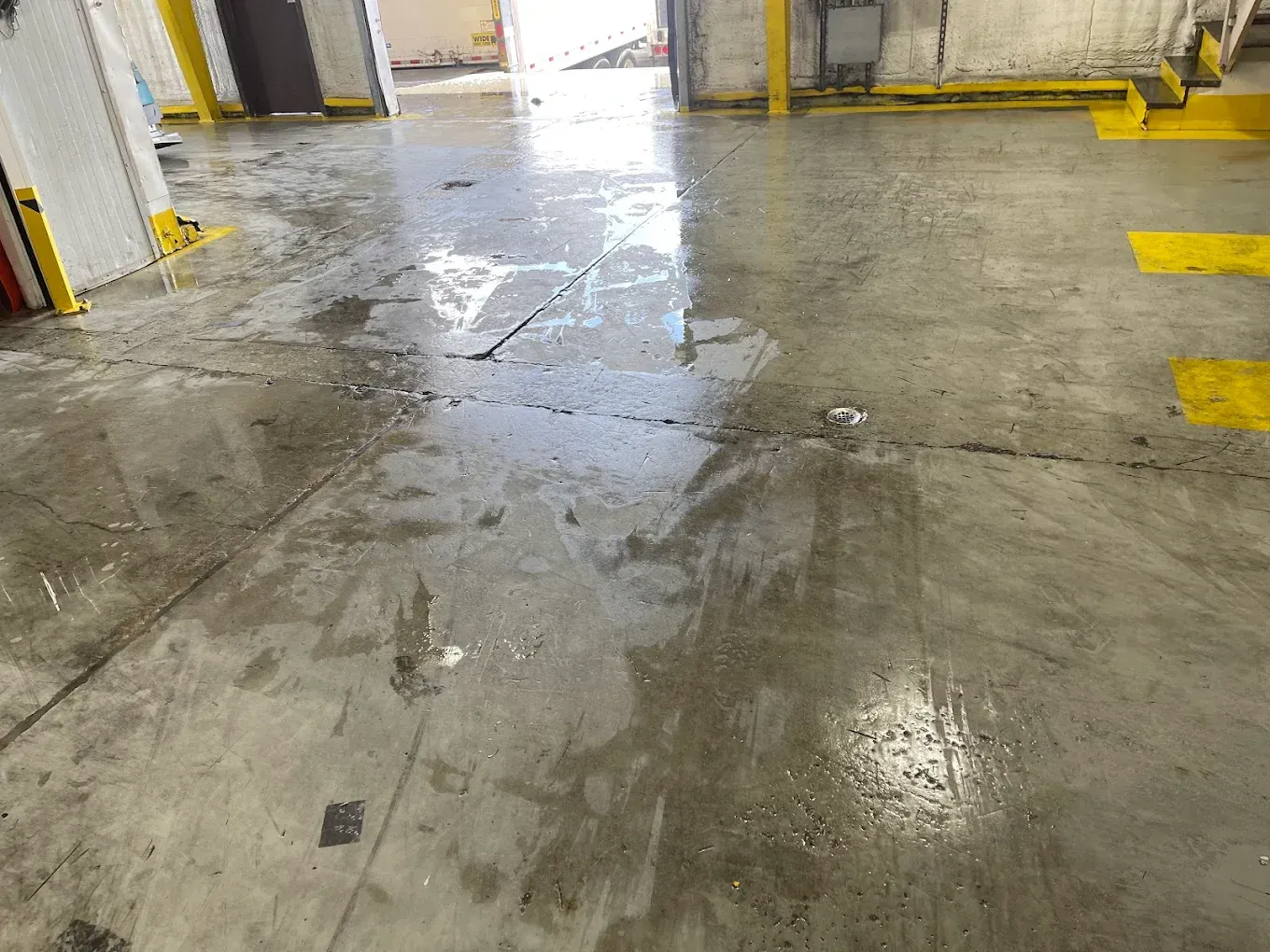 Wet concrete warehouse floor with reflective puddles and yellow floor markings near loading bays