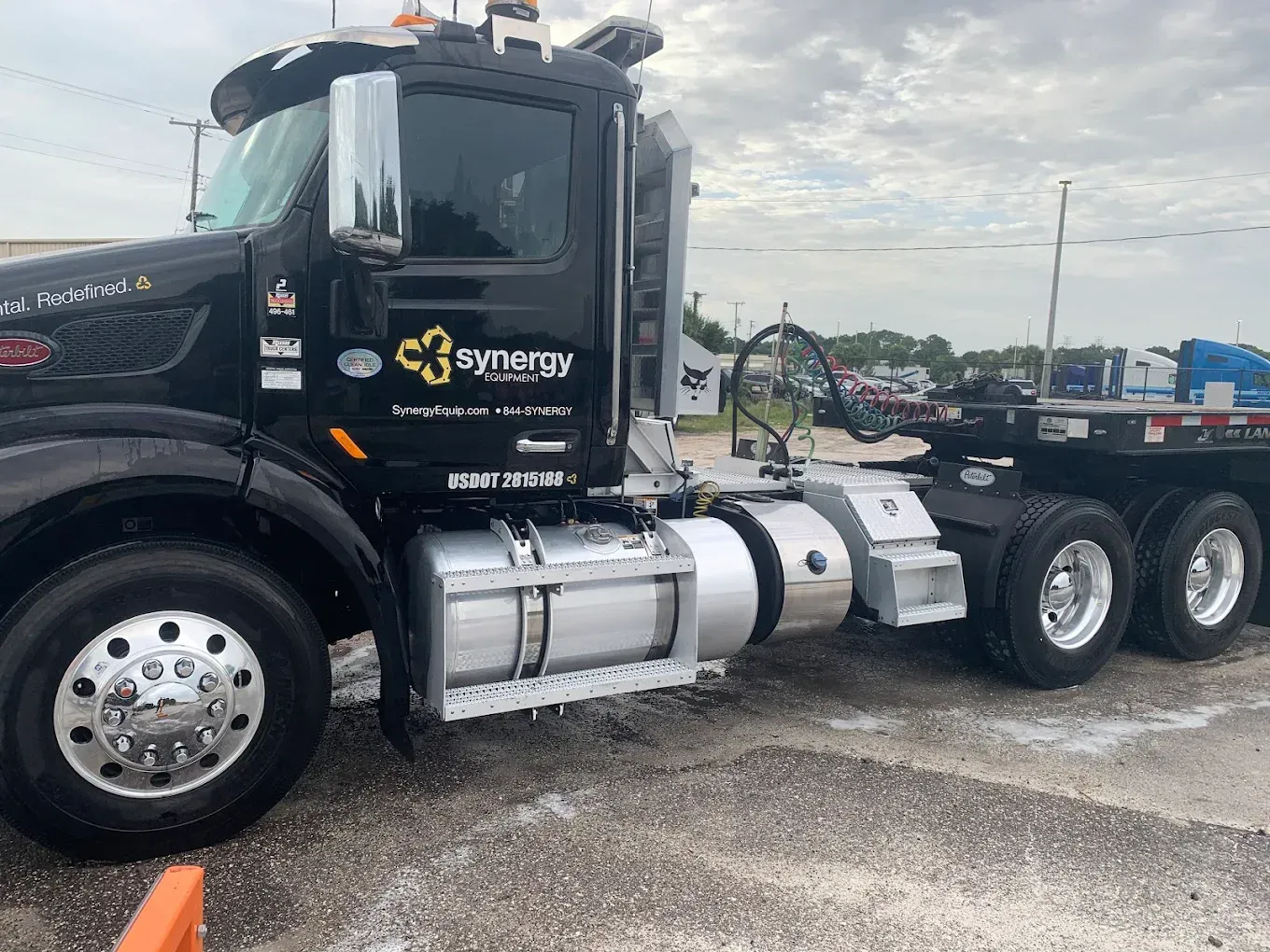 Black semi-truck tractor parked on wet pavement in an industrial lot