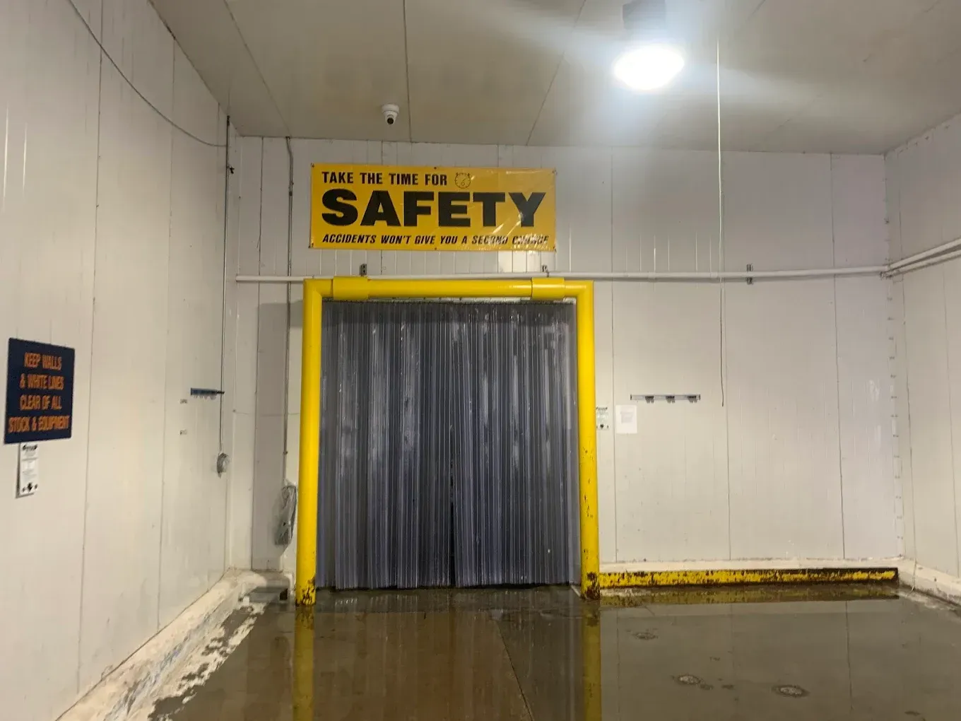 Yellow-framed industrial doorway with dark curtain and a safety sign above, in a clean warehouse room
