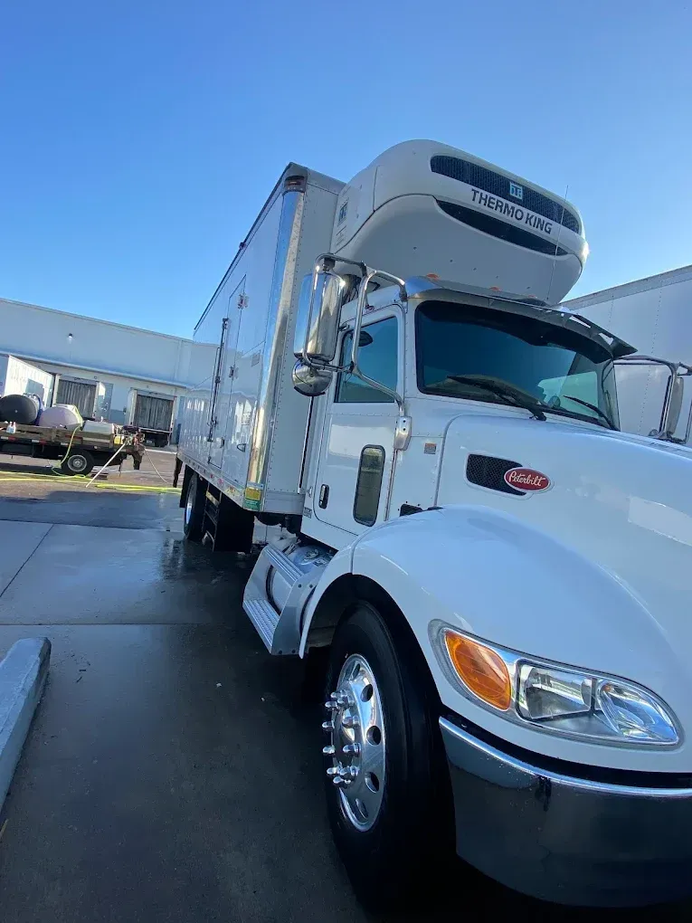 White semi-truck parked outdoors on a sunny day with a blue sky and industrial buildings nearby.