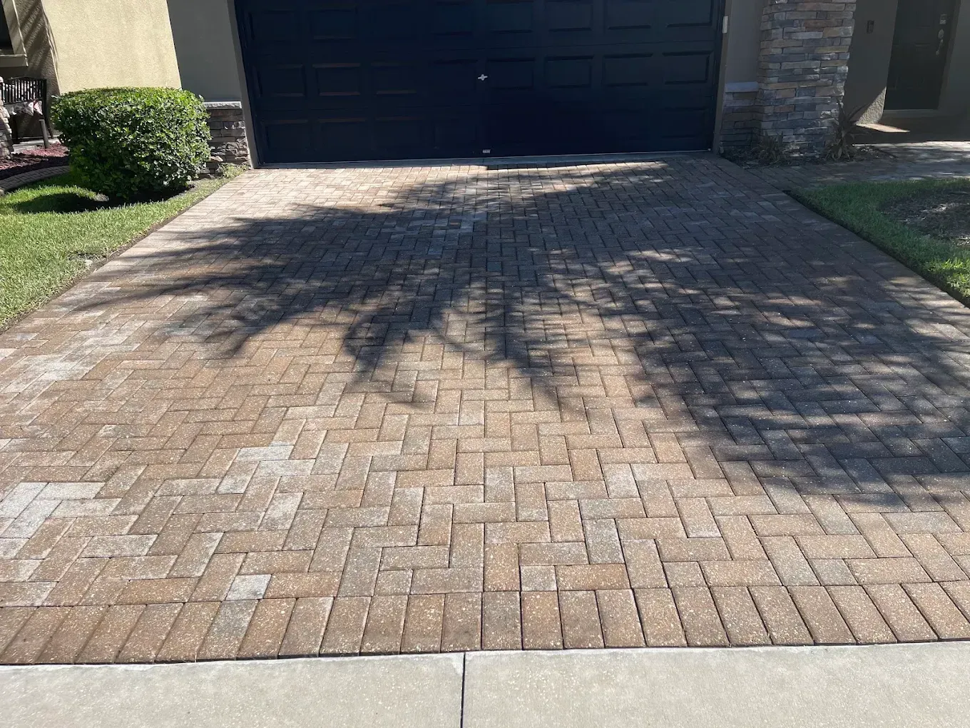 Brick driveway leading to a garage, with tree shadows across the pavement.