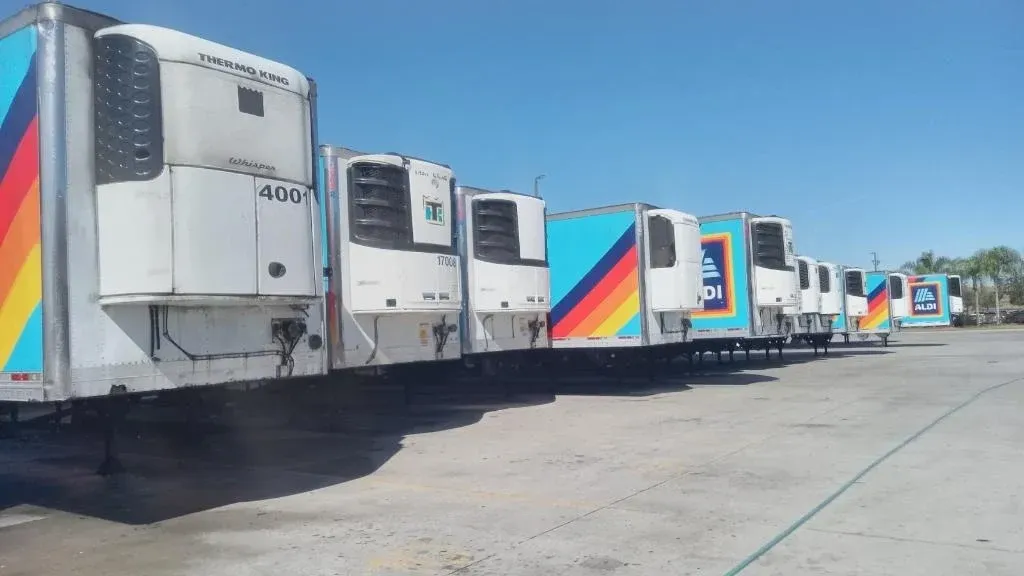 Row of white refrigerated trucks with rainbow stripes parked in a lot under a clear blue sky