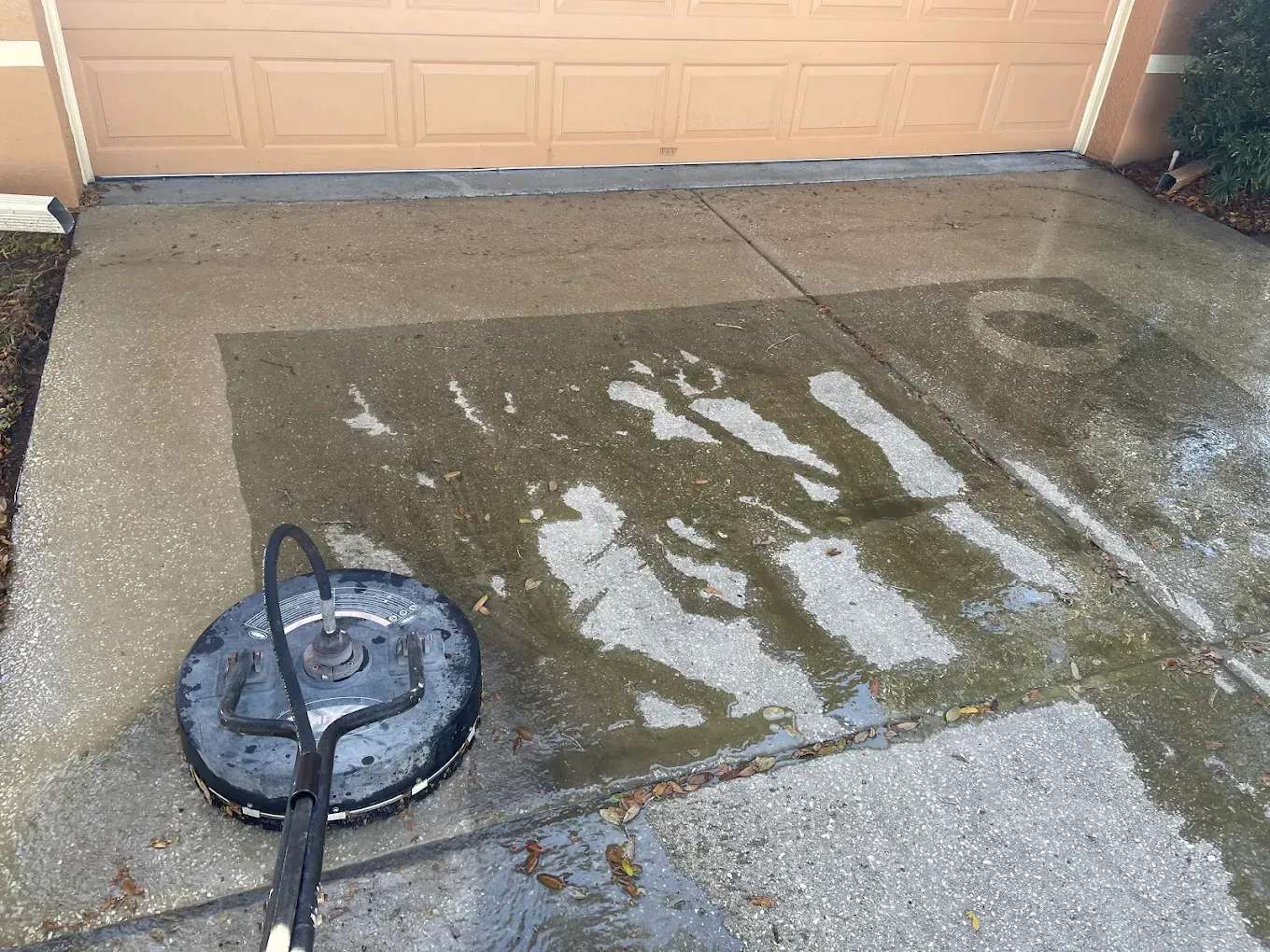 Concrete driveway being power washed near a garage door, with wet and clean patches visible.