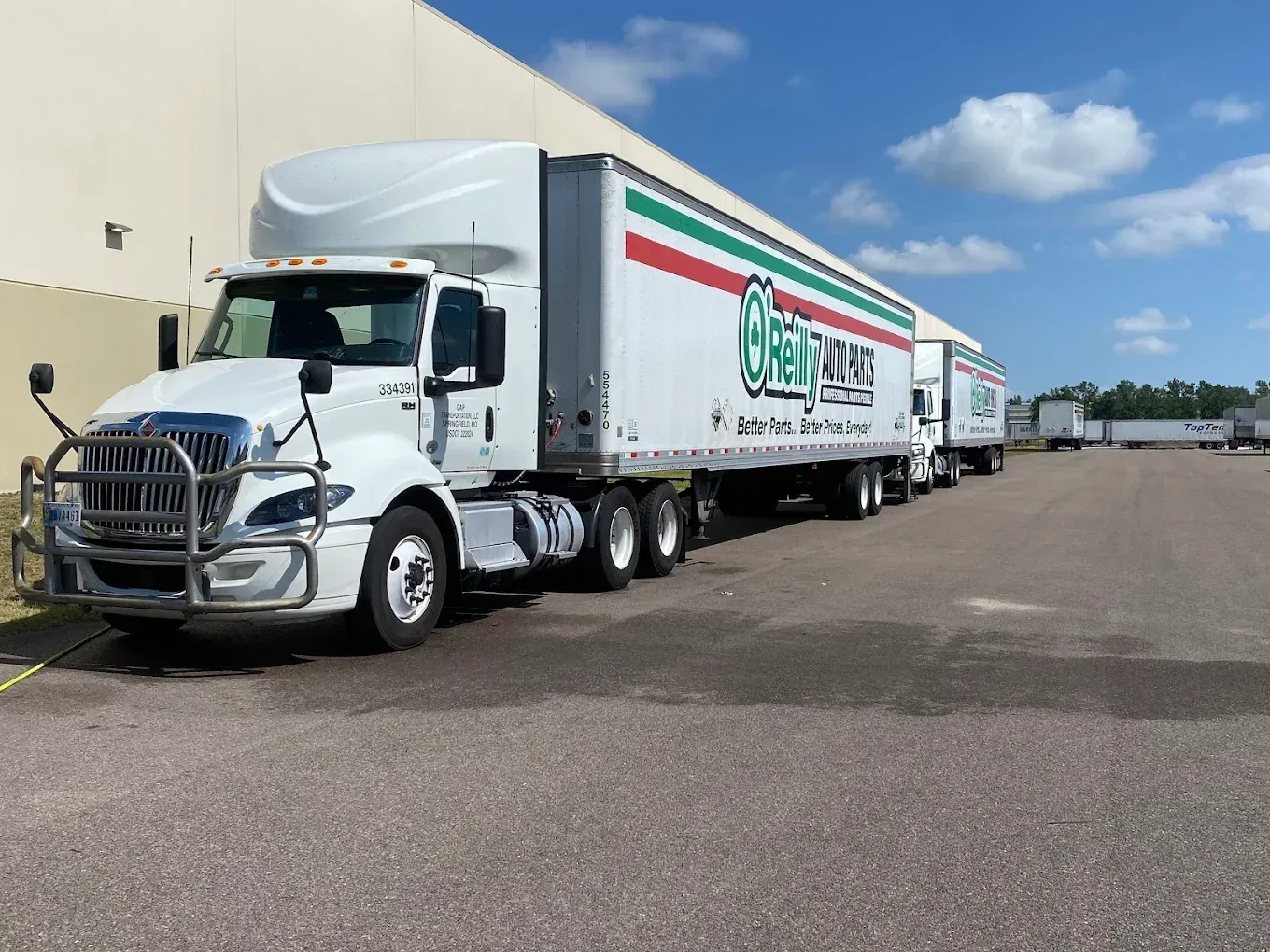 White semi-truck and trailer parked beside a warehouse under a blue sky.