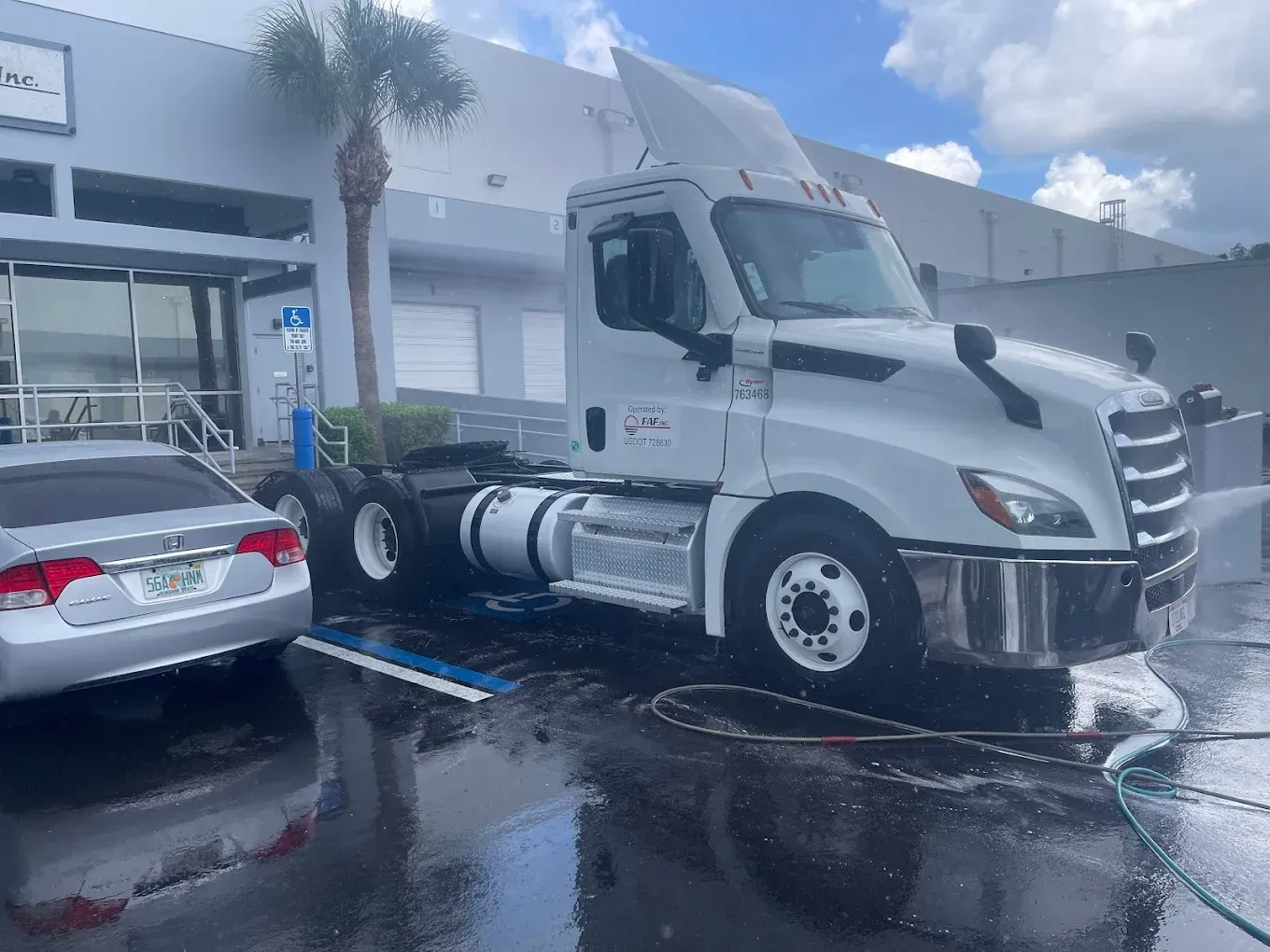 White semi-truck parked outside a storefront beside a wet silver sedan after rain