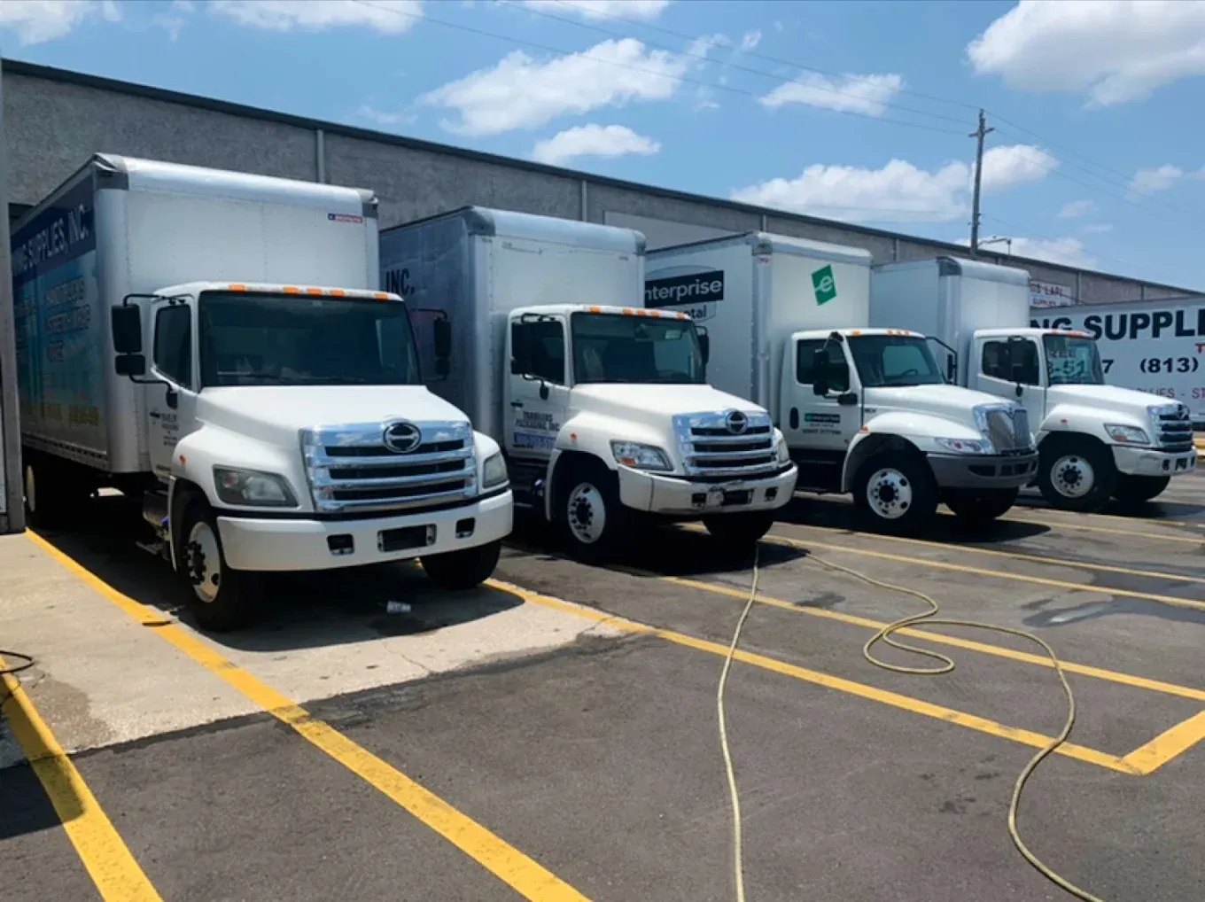 Three white delivery trucks parked outside a warehouse on a sunny day
