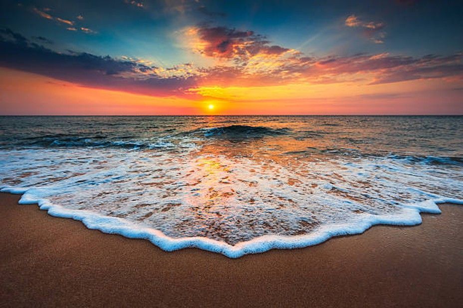 Sunset over the ocean with gentle waves washing onto a sandy beach.