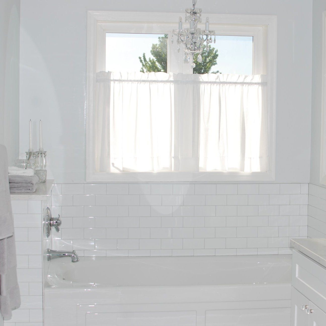 Bright white bathroom with a bathtub, subway-tile wall, and window above the tub.