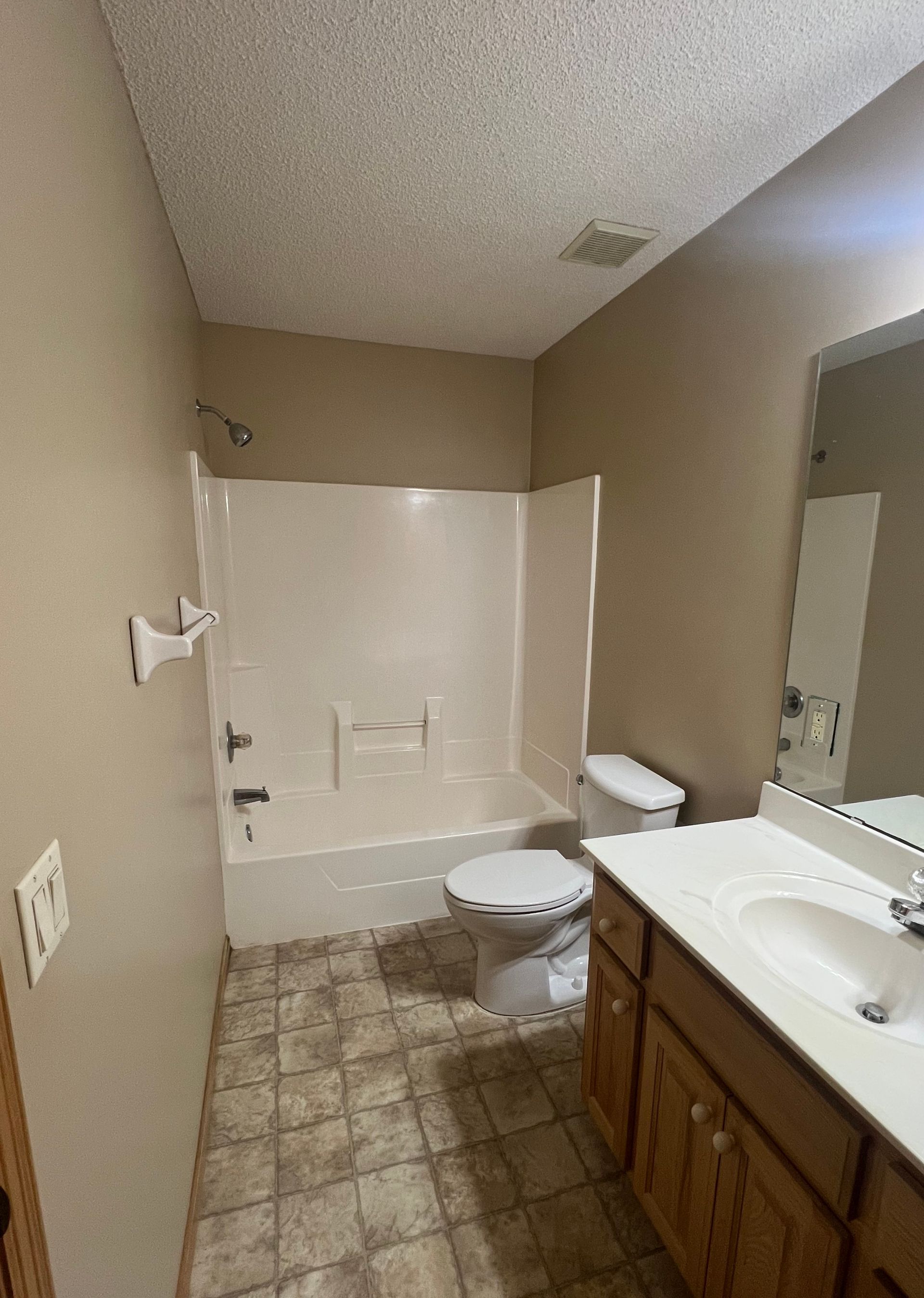 Small bathroom with a tub-shower, toilet, vanity sink, tan walls, and tiled floor.