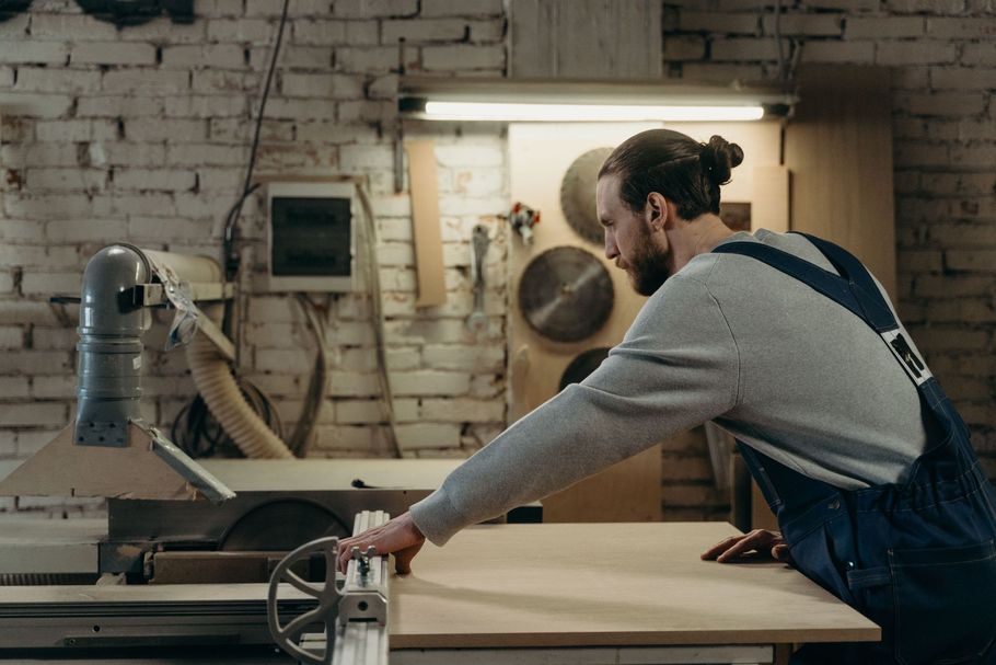 Man using a table saw in a woodshop, focused on cutting wood at a workbench.