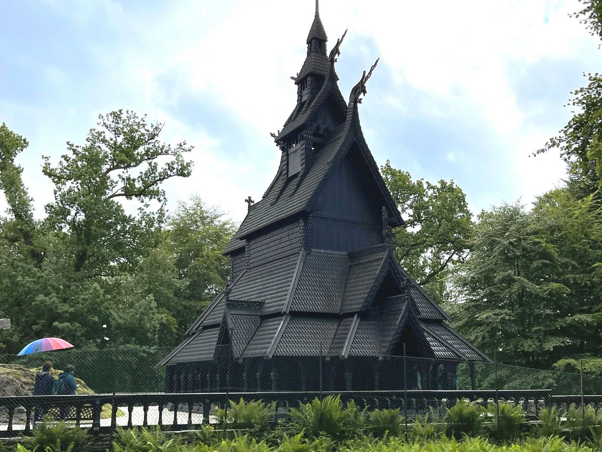 Fantoft Stave Church in Bergen, with dark timber walls and layered roofs framed by green trees.