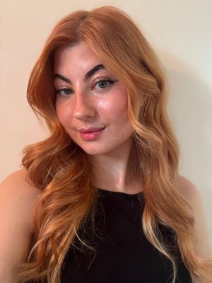 Portrait of a person with wavy blue hair, soft smile, and light makeup against a blurred cream background