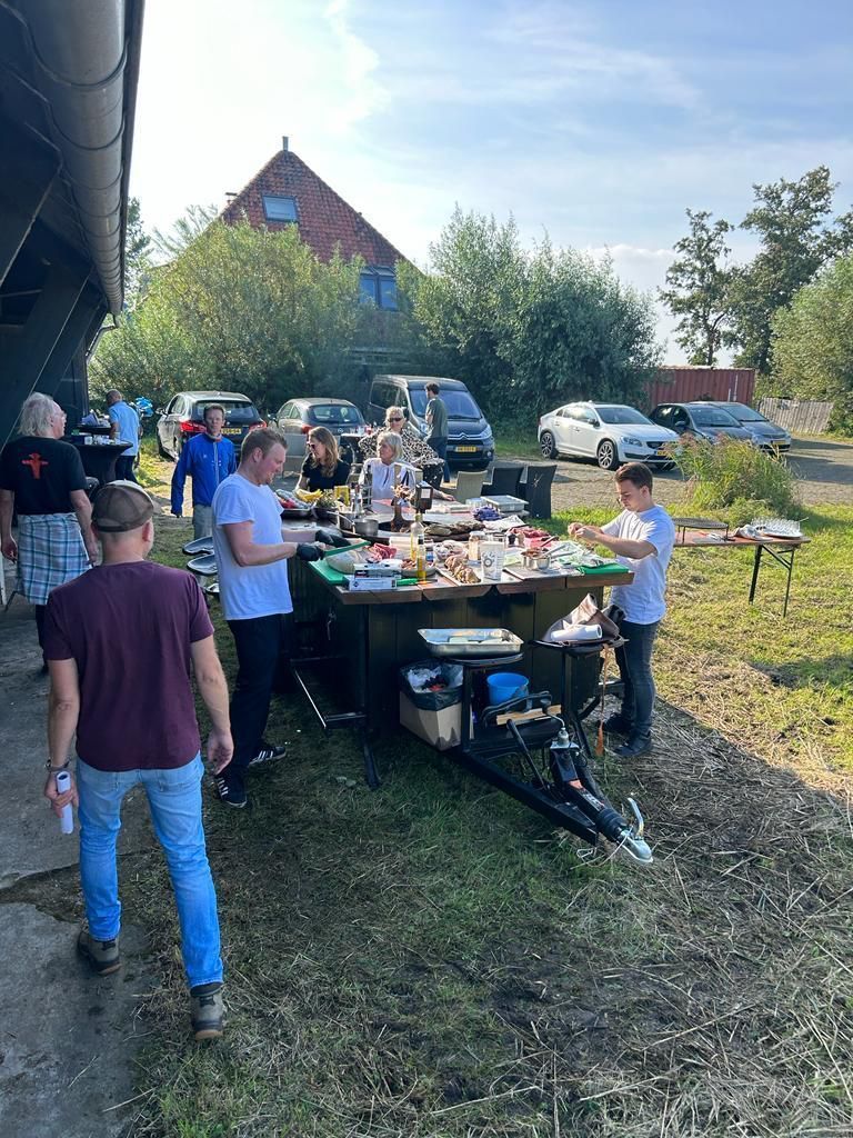 Mensen verzamelen zich buiten bij een trailer waar spullen uitgestald staan.