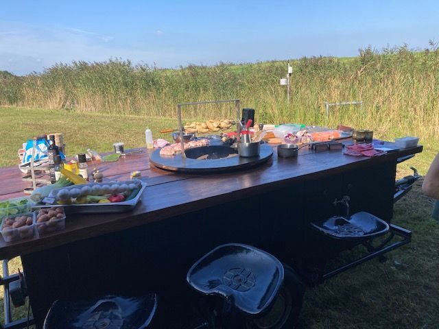 Buitenkeuken met grill, eten, zitgelegenheid en riet op de achtergrond op een zonnige dag.