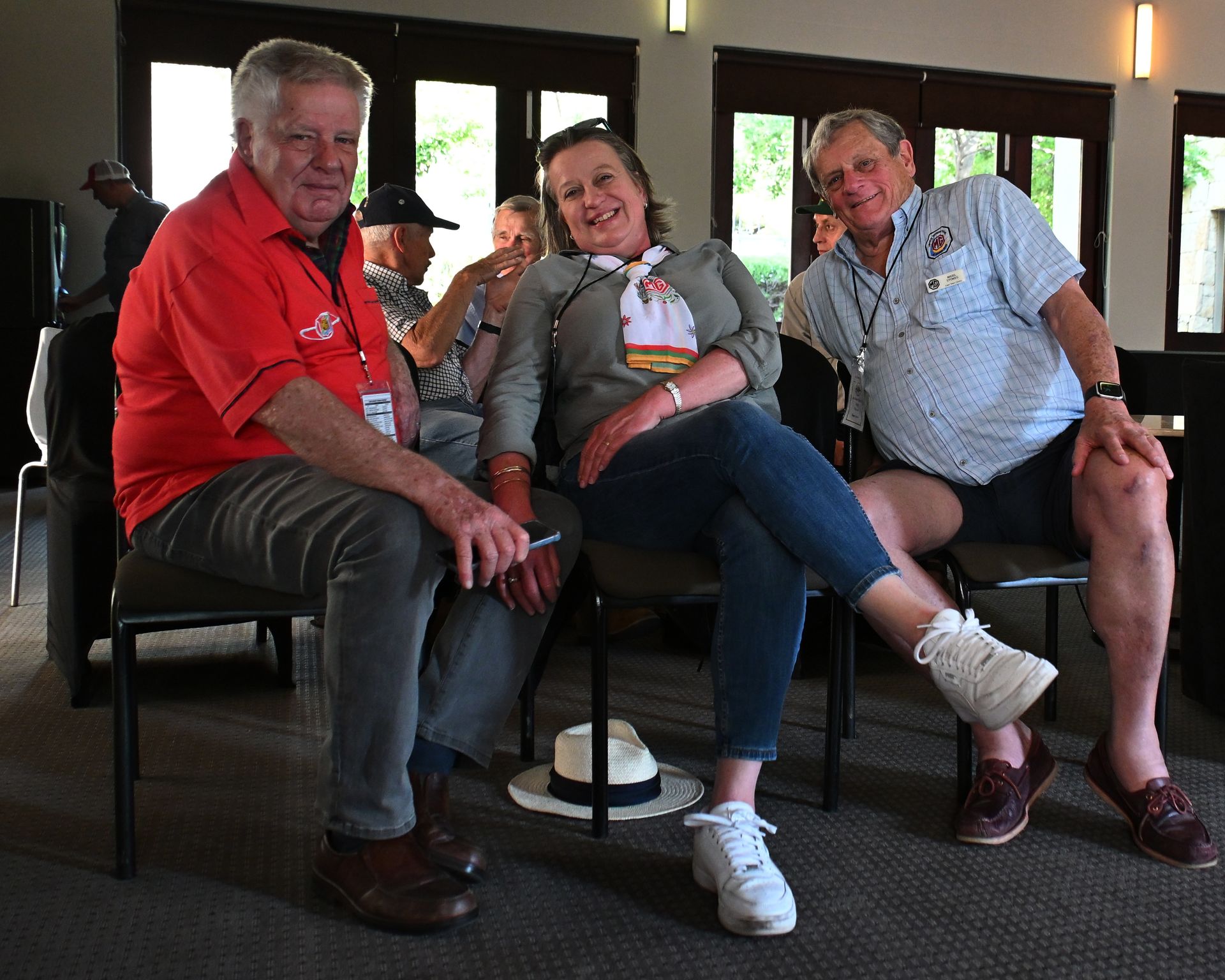 Three smiling people sit on chairs in a bright indoor lounge.