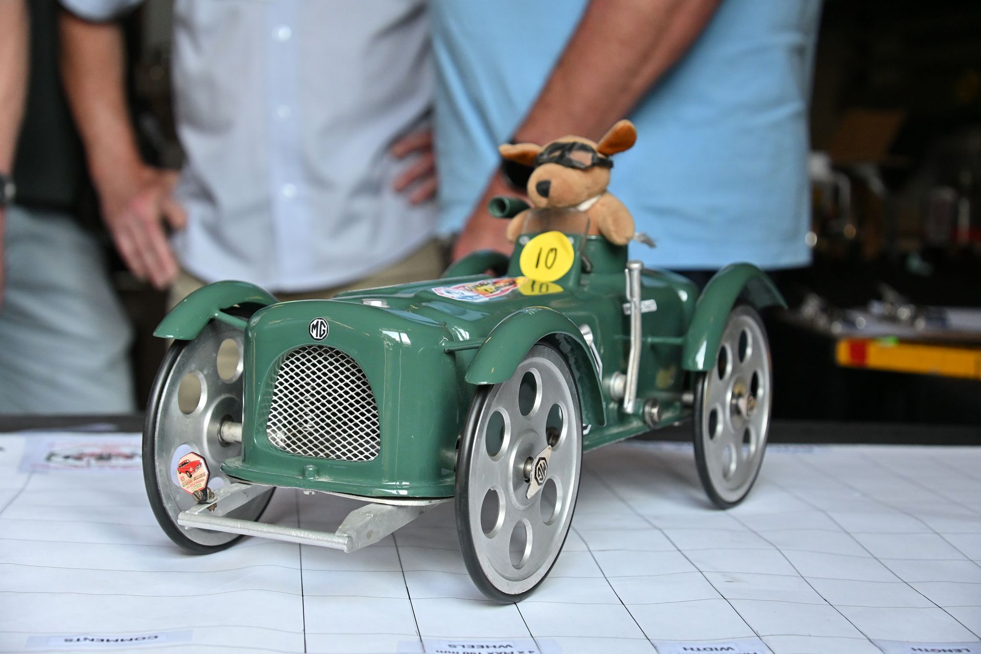 Green toy car with a stuffed dog driver, displayed on a tiled floor