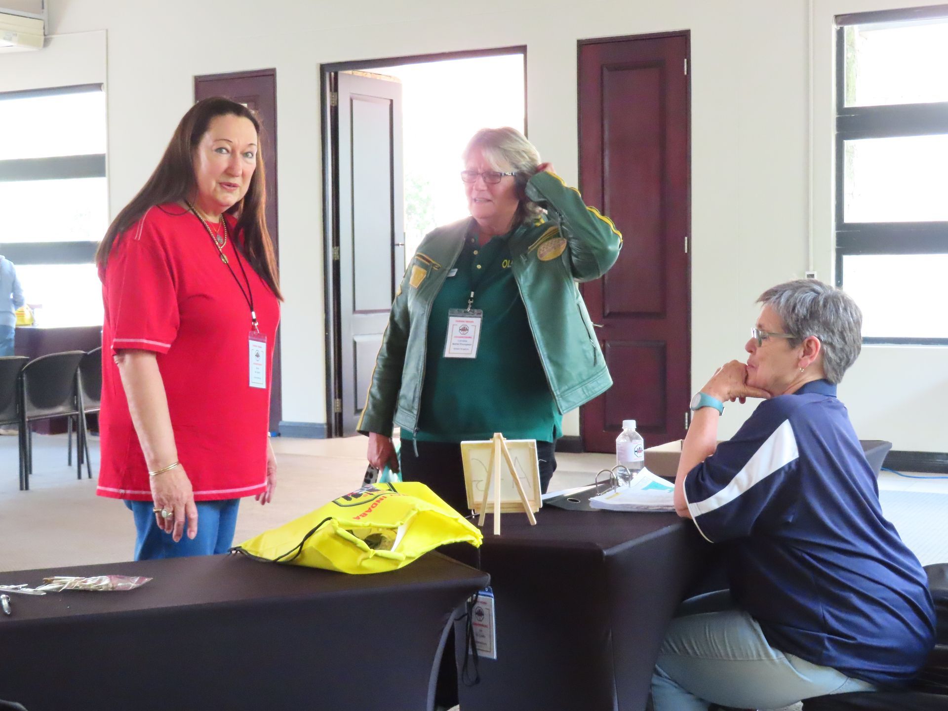 Three people talking around a table in a bright room, with folders and a water bottle on the table.