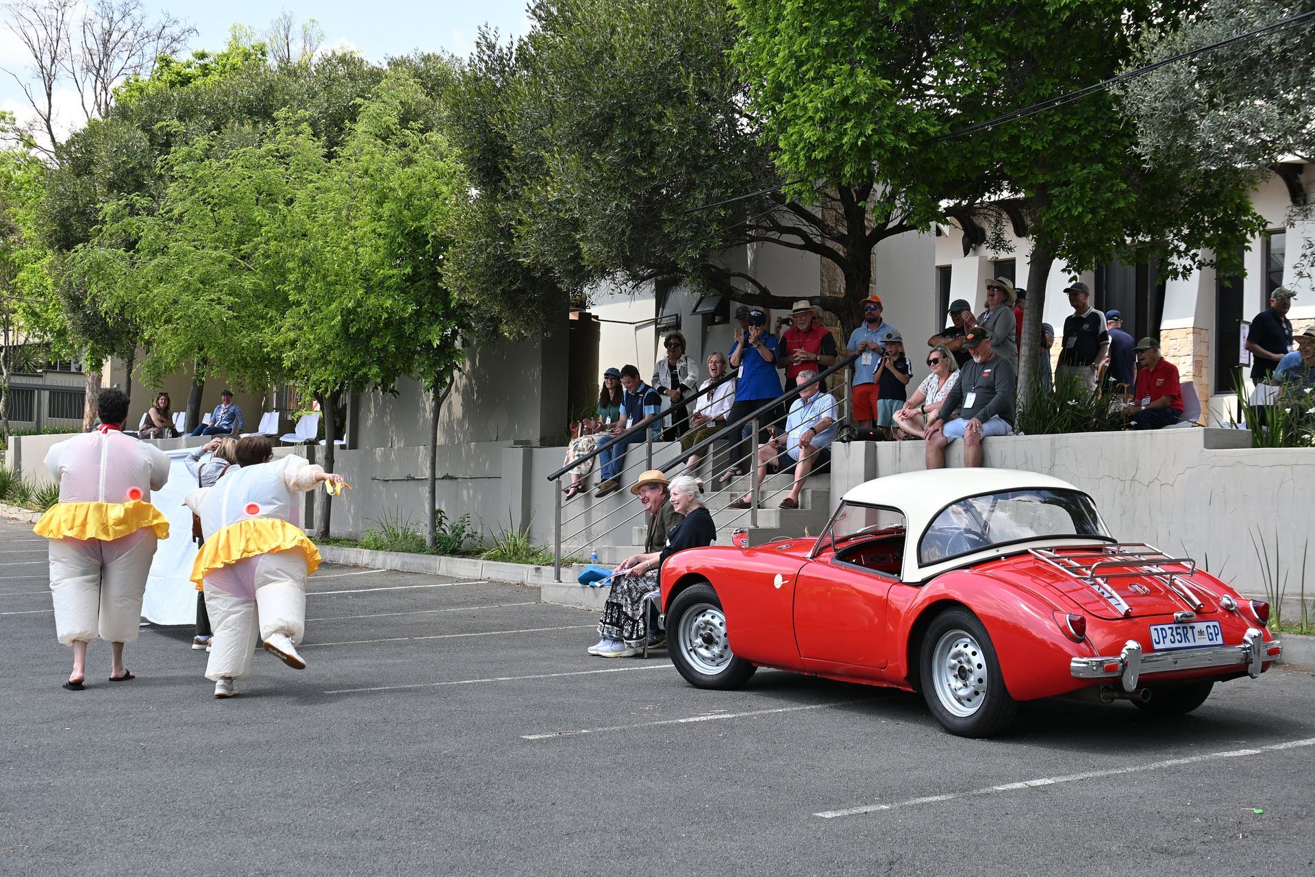 Red vintage convertible driving past spectators on a tree-lined street during a parade