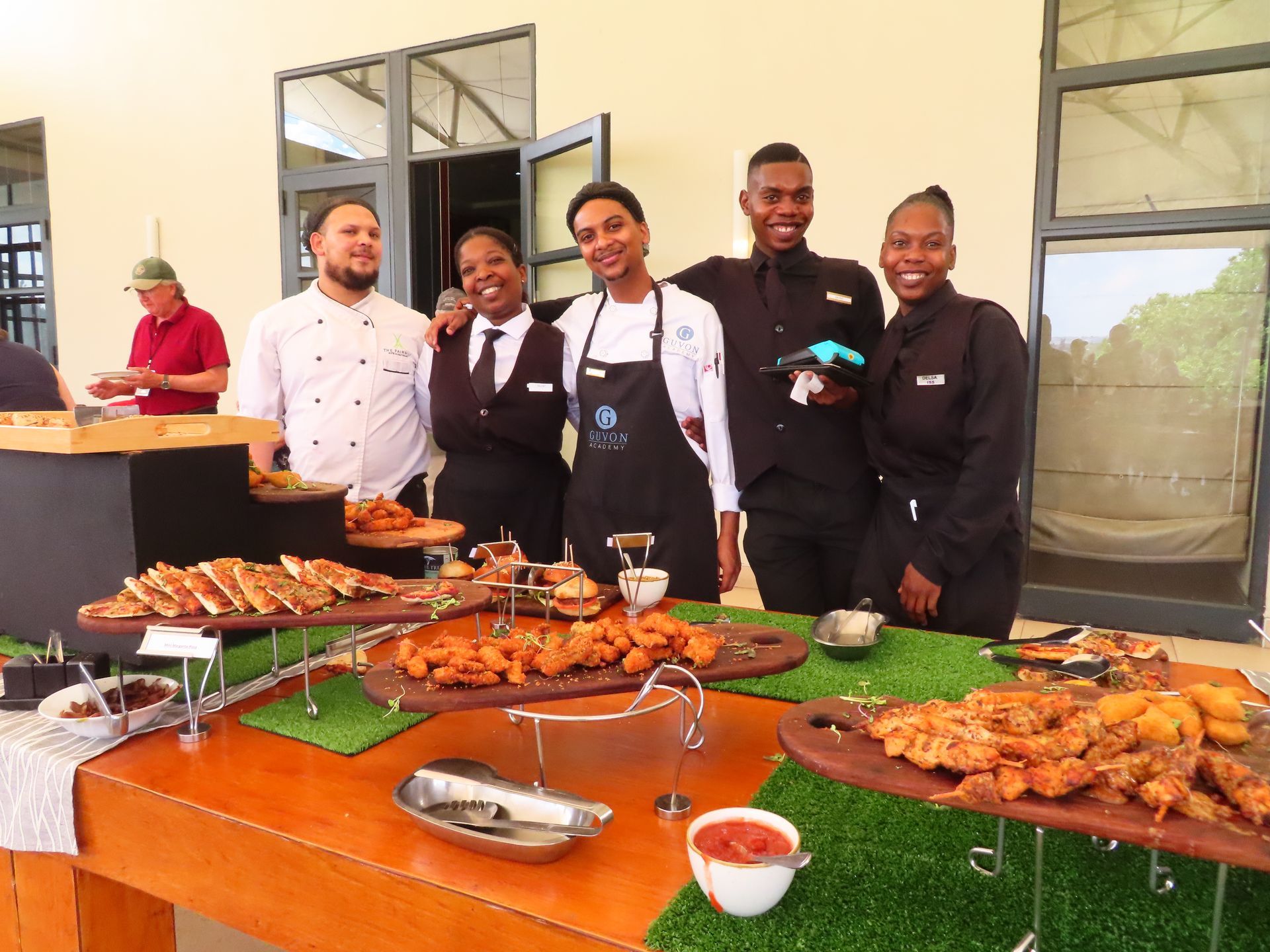 Chefs and staff posing behind a buffet table with trays of grilled food in a bright dining area
