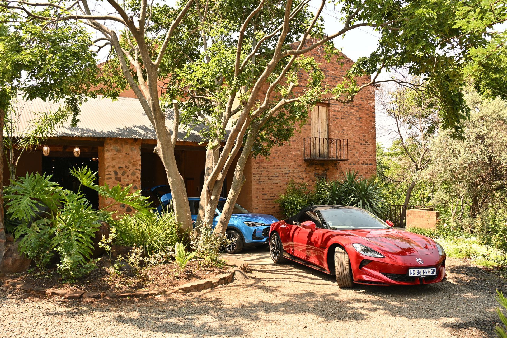 Brick house driveway with two sports cars, a red one in front and a blue one under trees