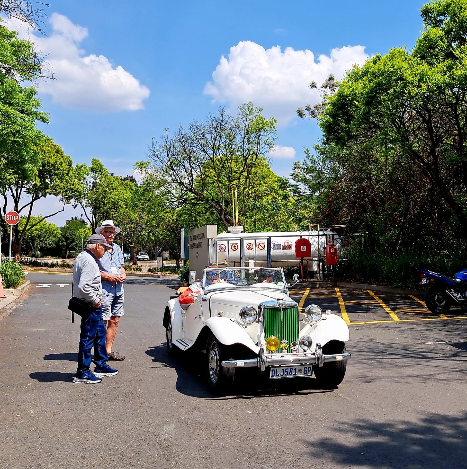 White vintage car with floral decorations parked outdoors beside two people on a sunny day