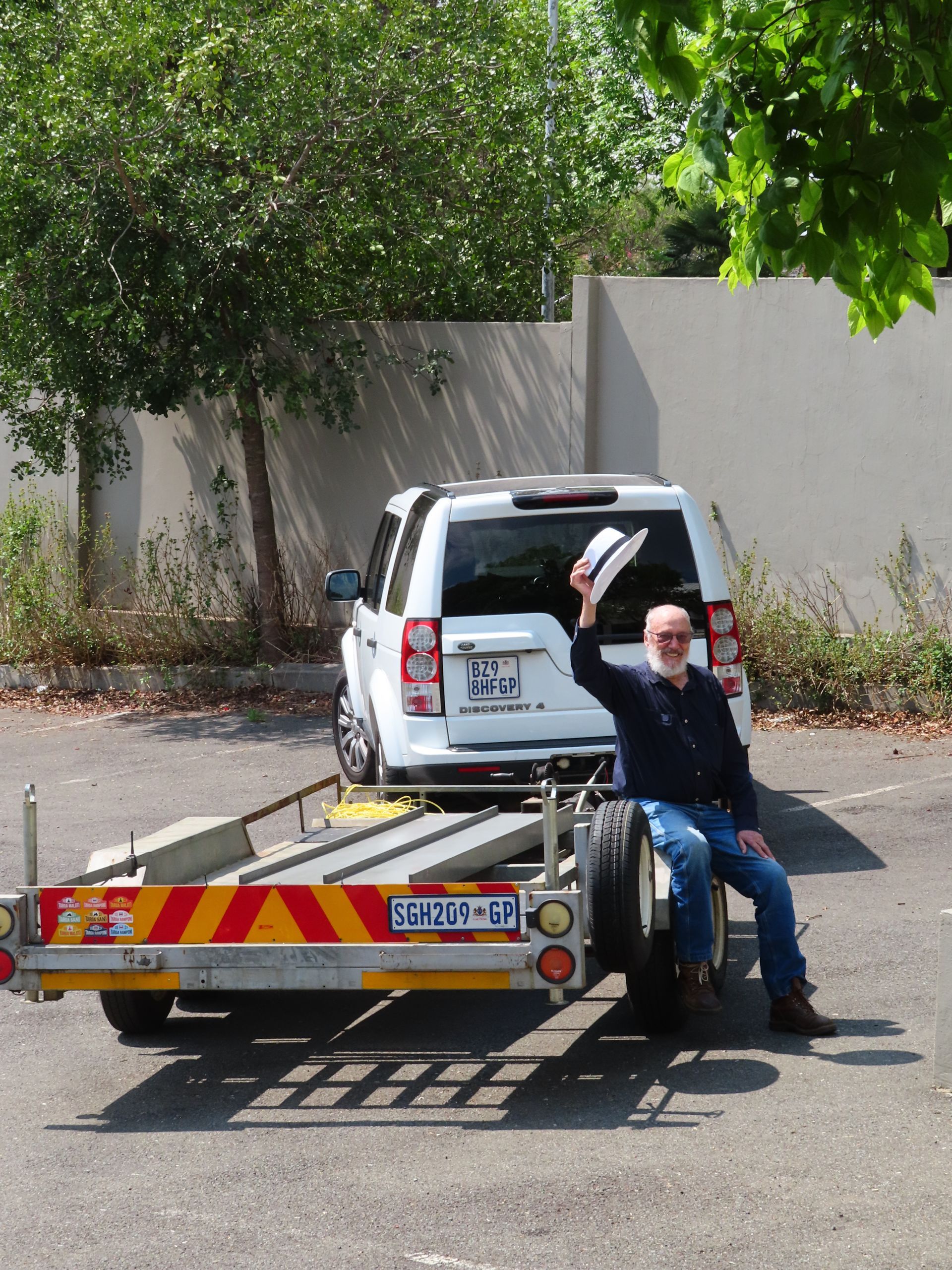 Person sitting on a flatbed tow truck, waving beside a white SUV parked on a roadside.
