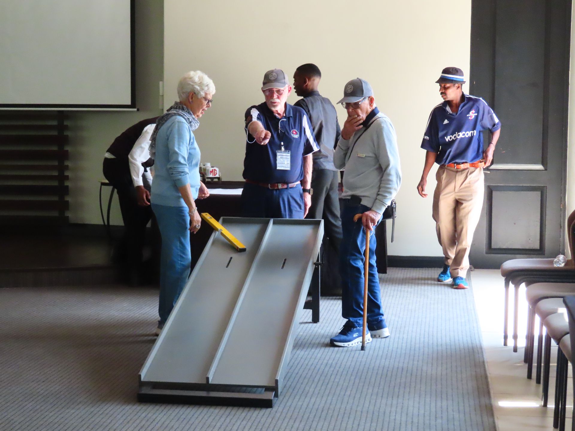 Group in a room watching a person test a wheelchair ramp with a cane
