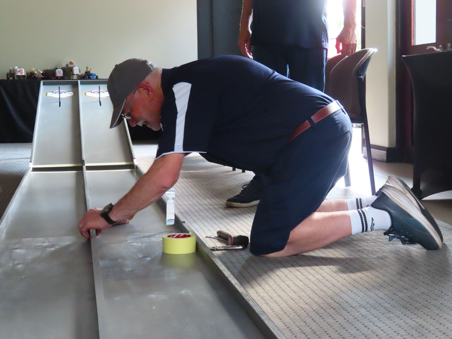 Person kneeling on a floor, measuring along a long strip with a tape measure in a bright room