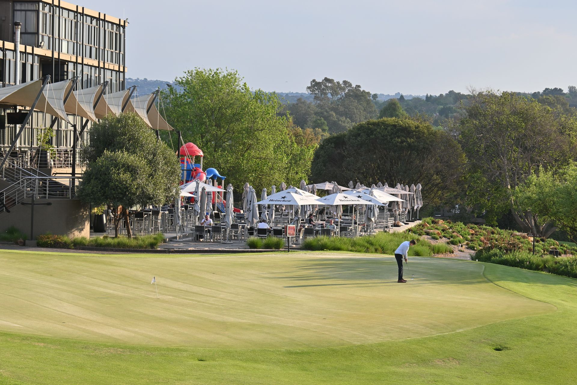 Golfer on a green overlooking a clubhouse and outdoor event tents on a sunny day