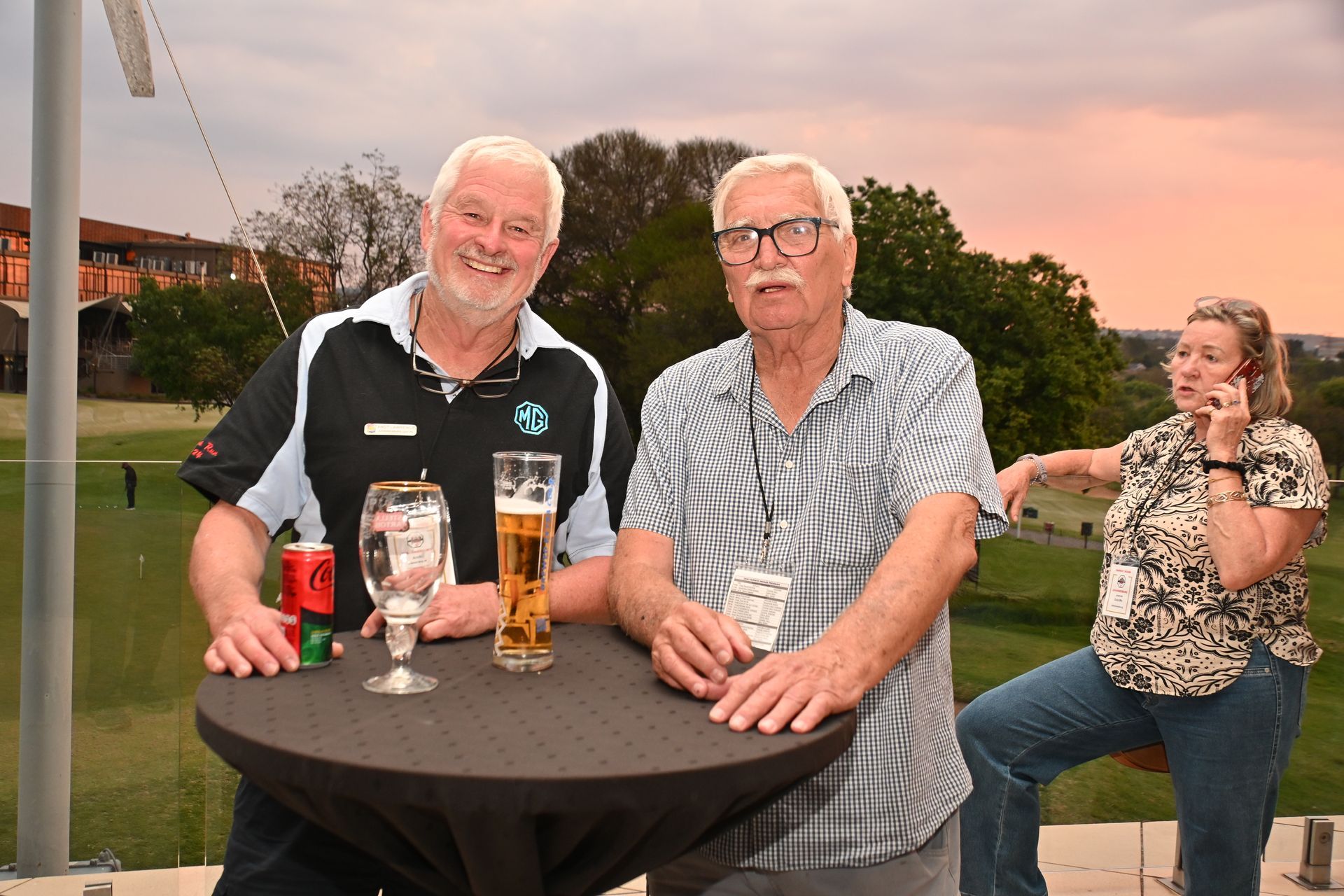 Three people seated at an outdoor table with drinks at sunset, smiling and chatting.