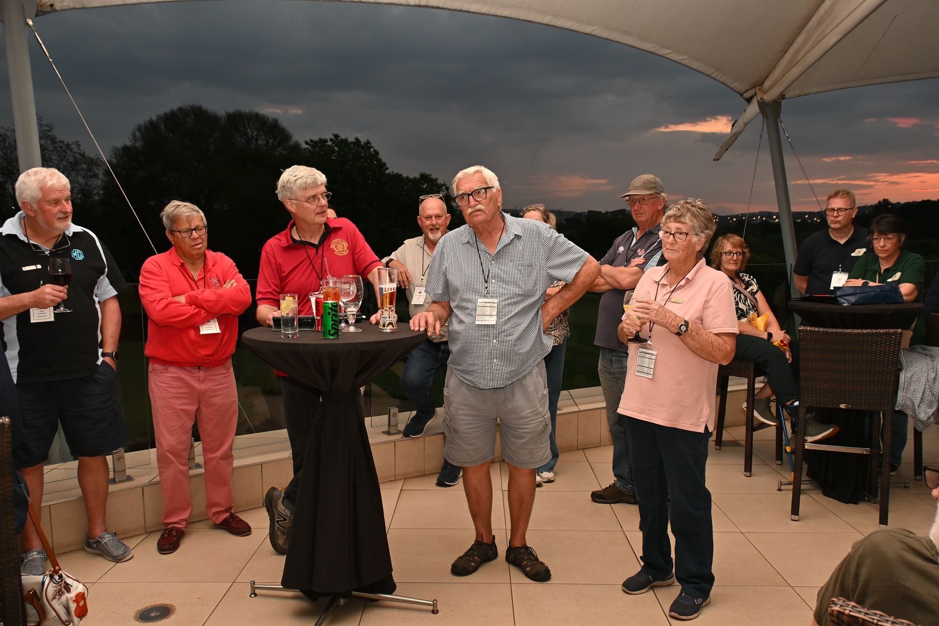 People standing and talking at an outdoor gathering under a canopy at dusk