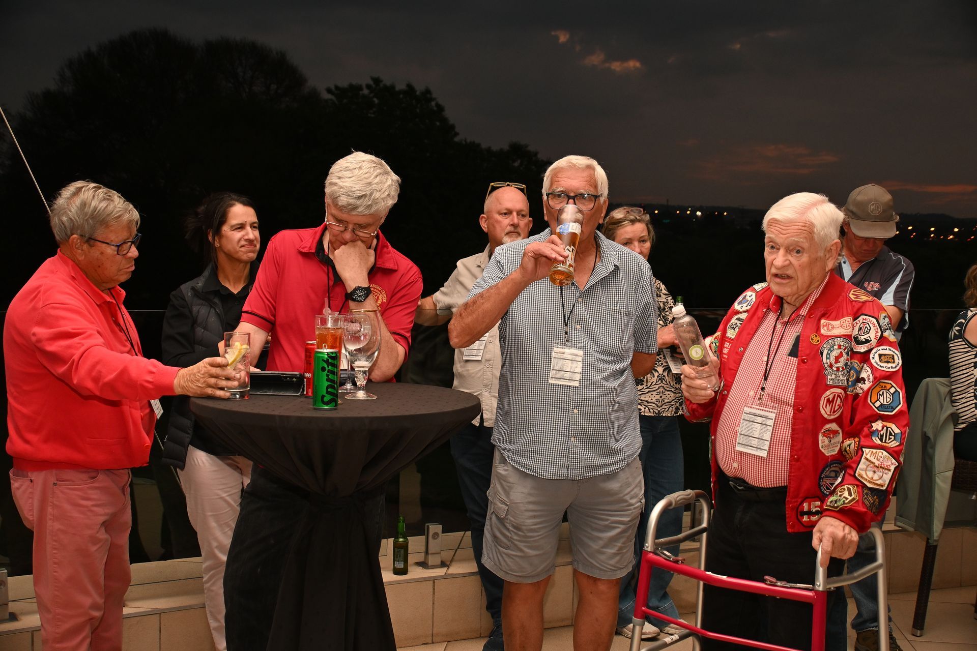 Guests chatting and raising drinks around a tall table at a dimly lit party event