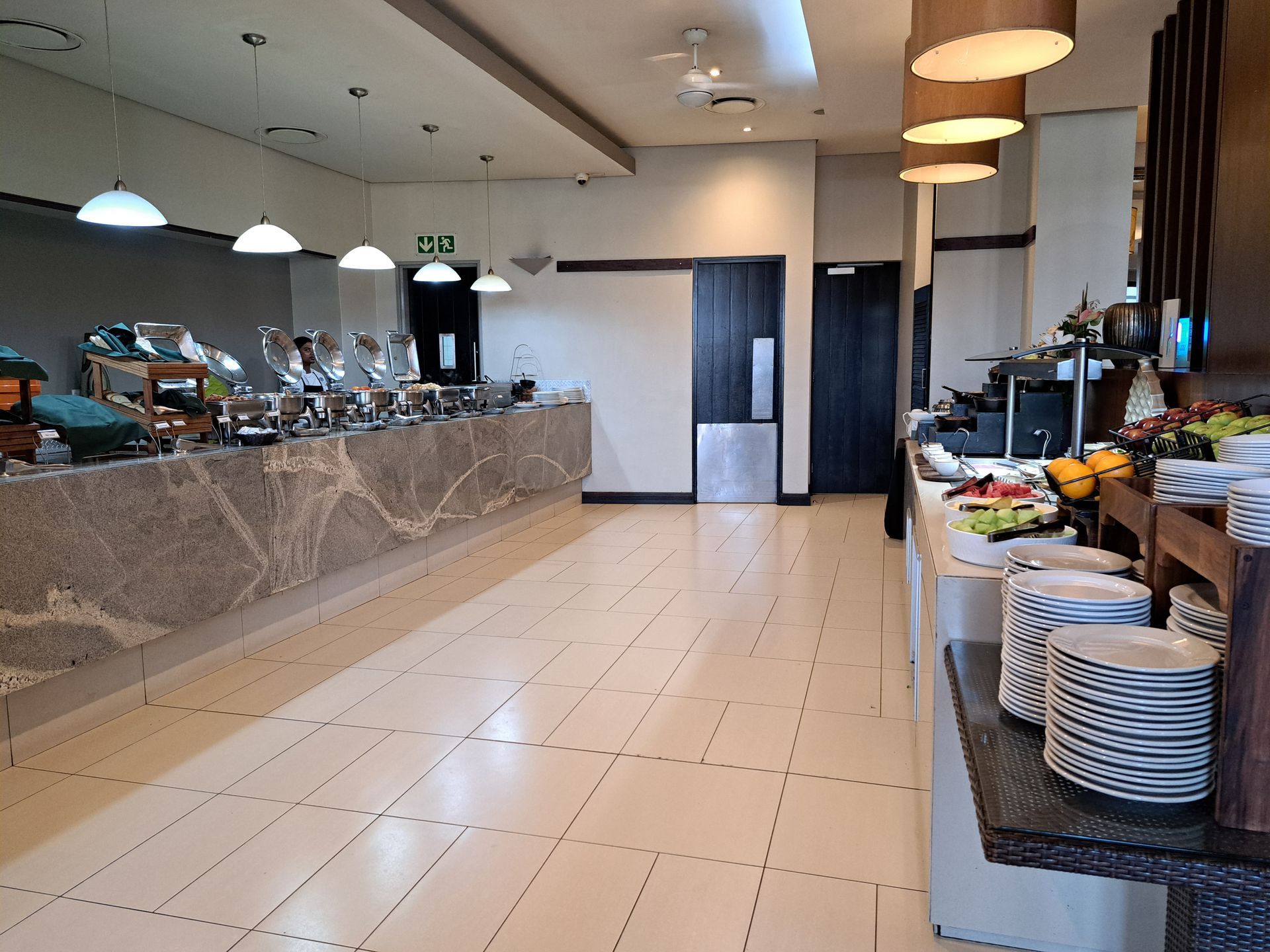 Empty restaurant buffet area with tiled floor, hanging lights, and serving dishes on counters