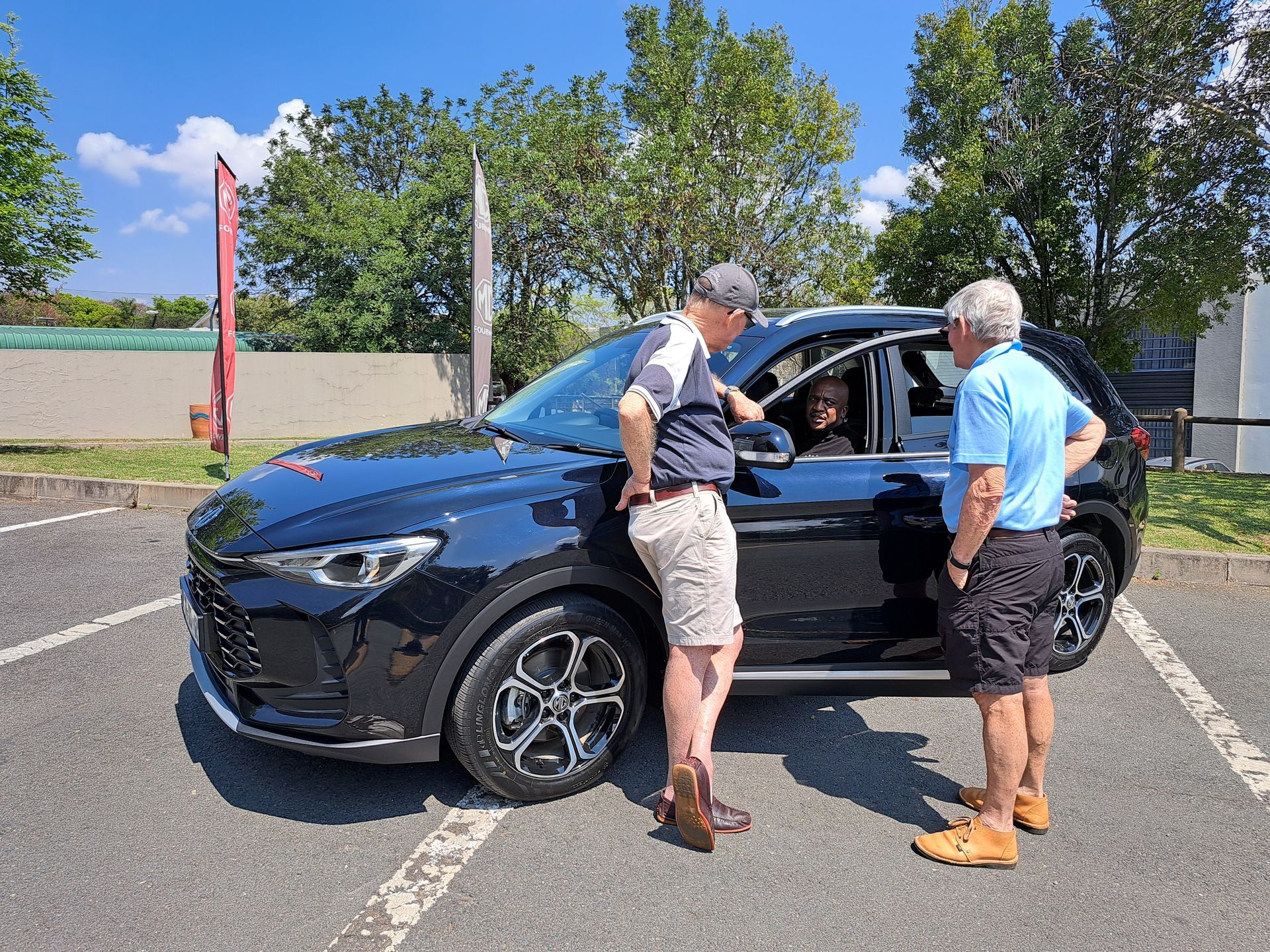 Two men talking beside a black SUV in a parking lot on a sunny day