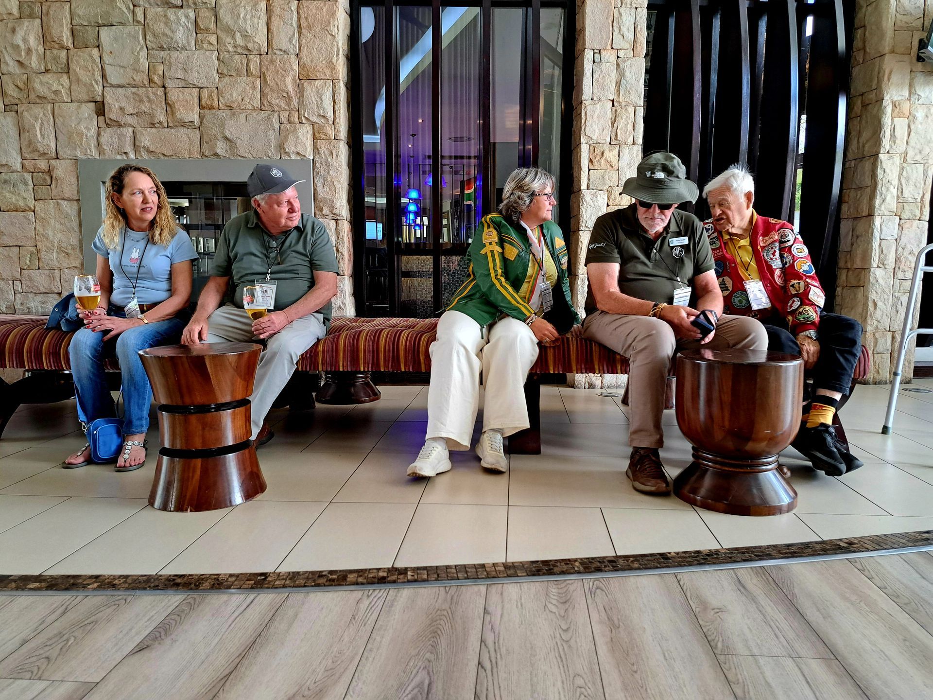 Five people sit on wooden stools in a lobby, chatting in front of large windows.