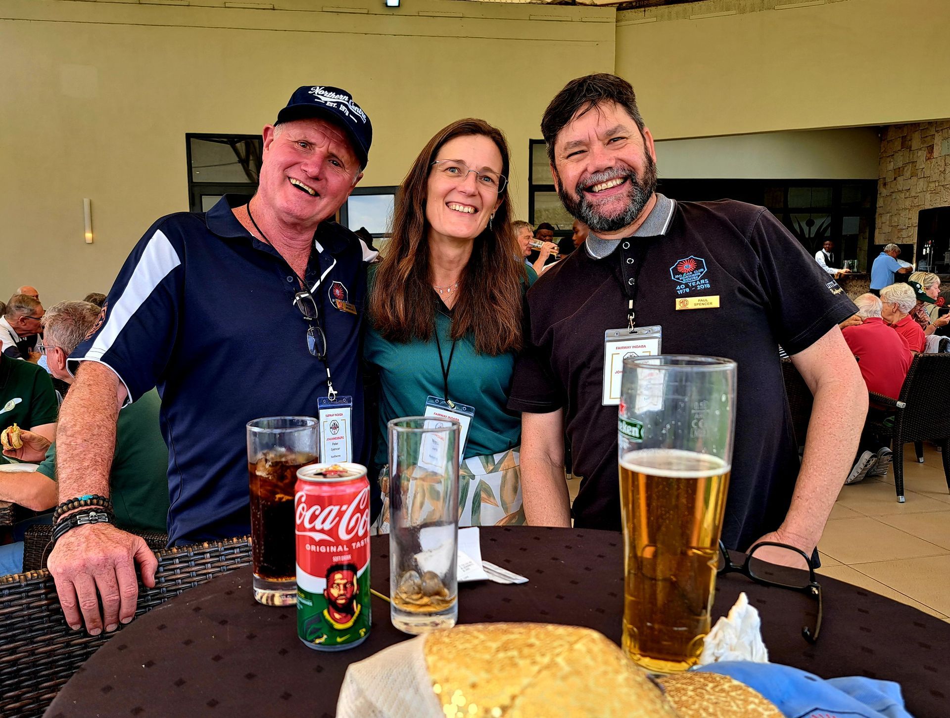 Three people smiling at a table with drinks and food at a casual indoor event