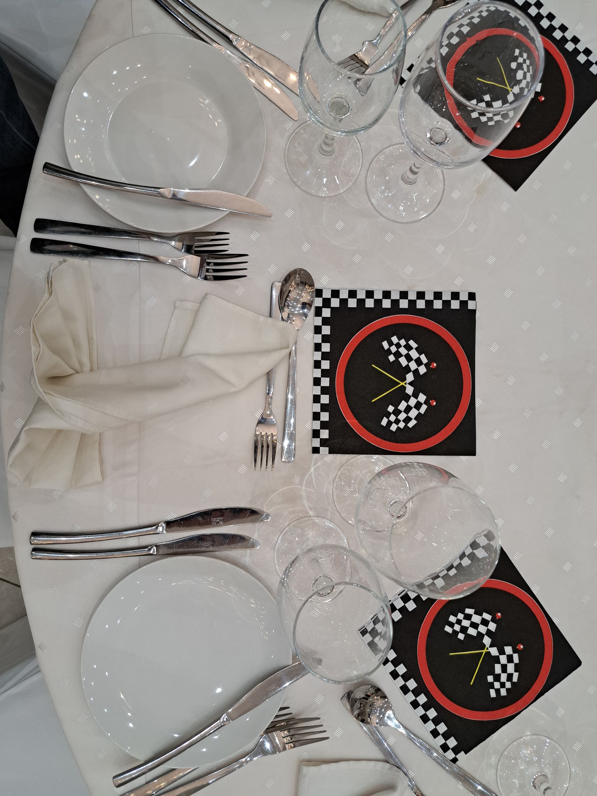 Elegant dining table set with white plates, silverware, glasses, and black checkered napkins with red chargers