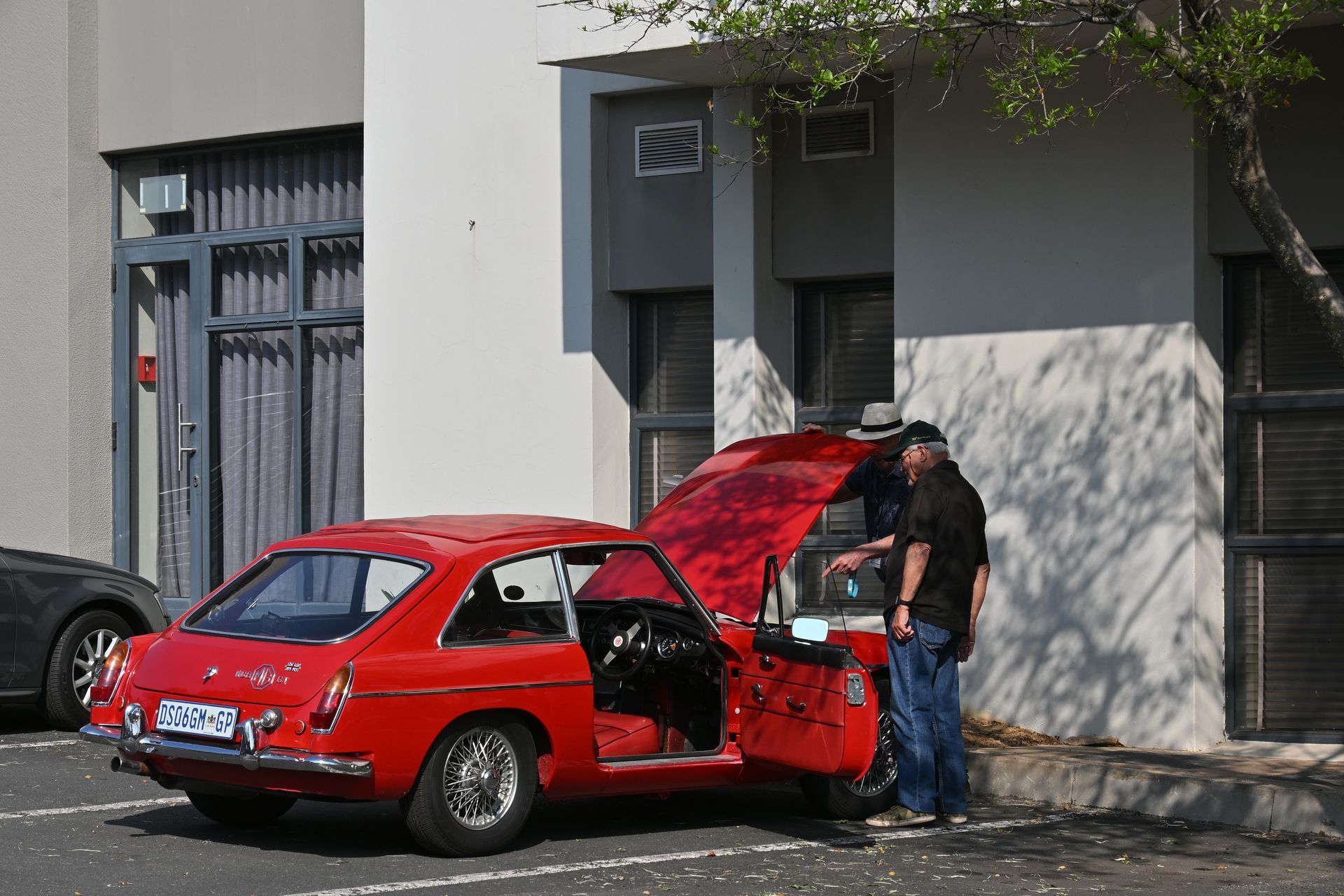 Man standing beside a red car with its hood and door open on a city street