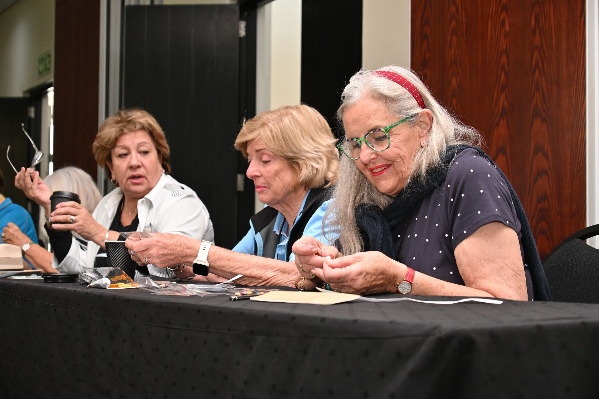Three people seated at a table, reading papers during a meeting or panel discussion.