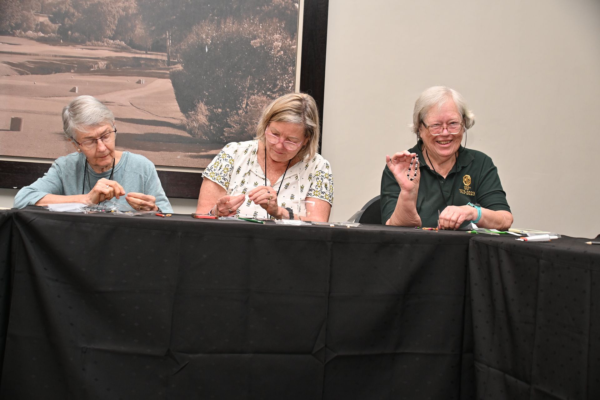 Three people seated behind a black table at a panel, with one speaking into a microphone.