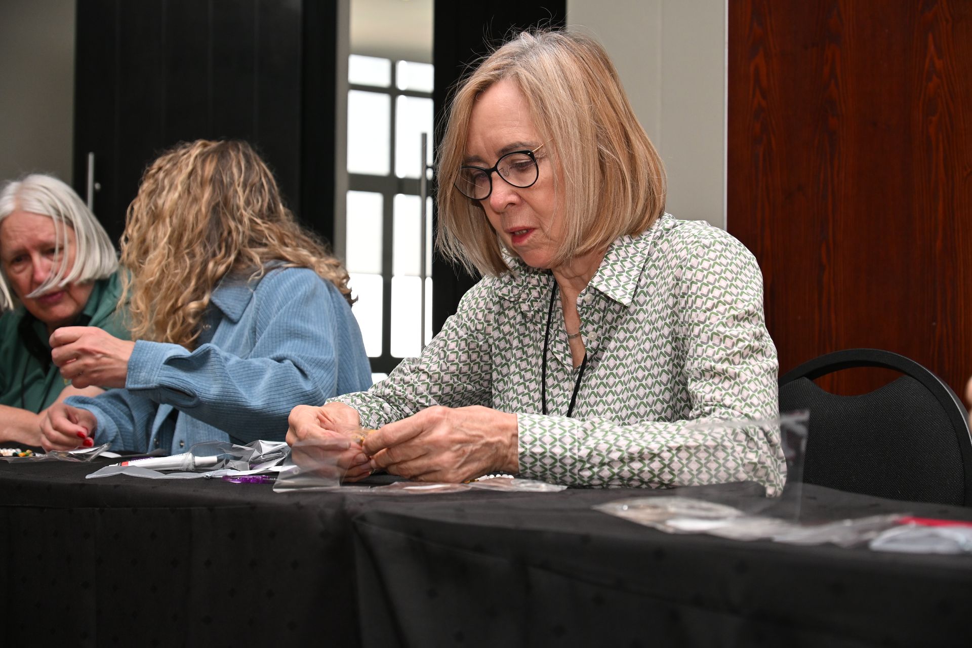 Three people seated at a table, writing in a conference room with wood-paneled walls.