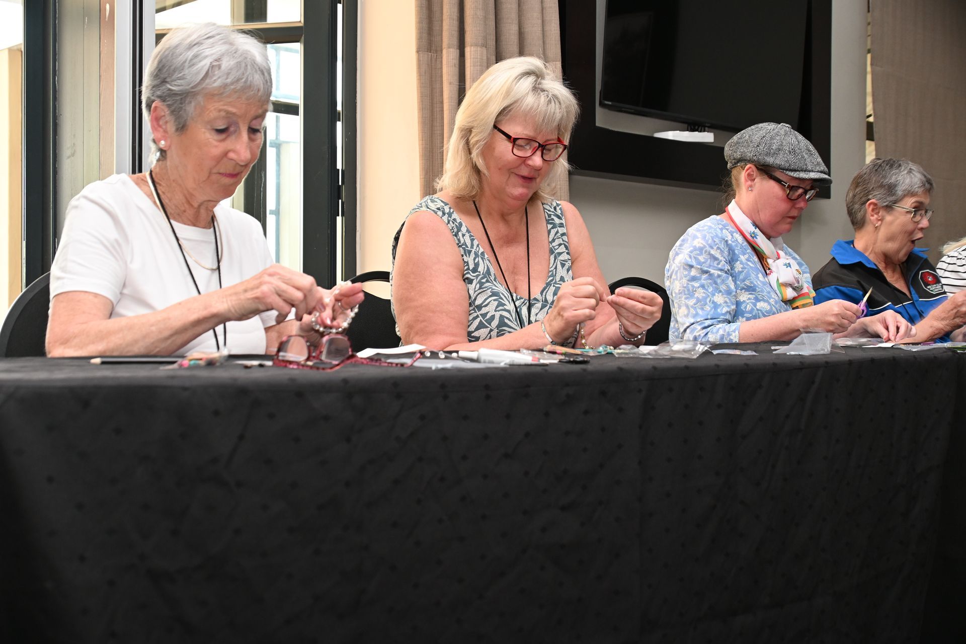 Four people seated at a table, concentrating on their craftwork during a workshop