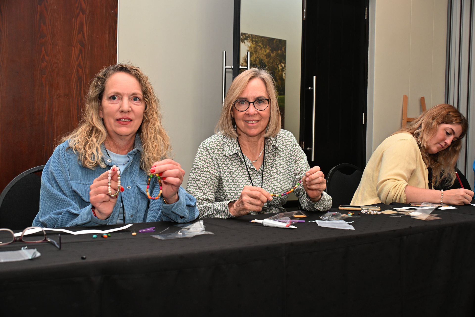 Three people seated at a table, handling small items during a workshop or registration event.