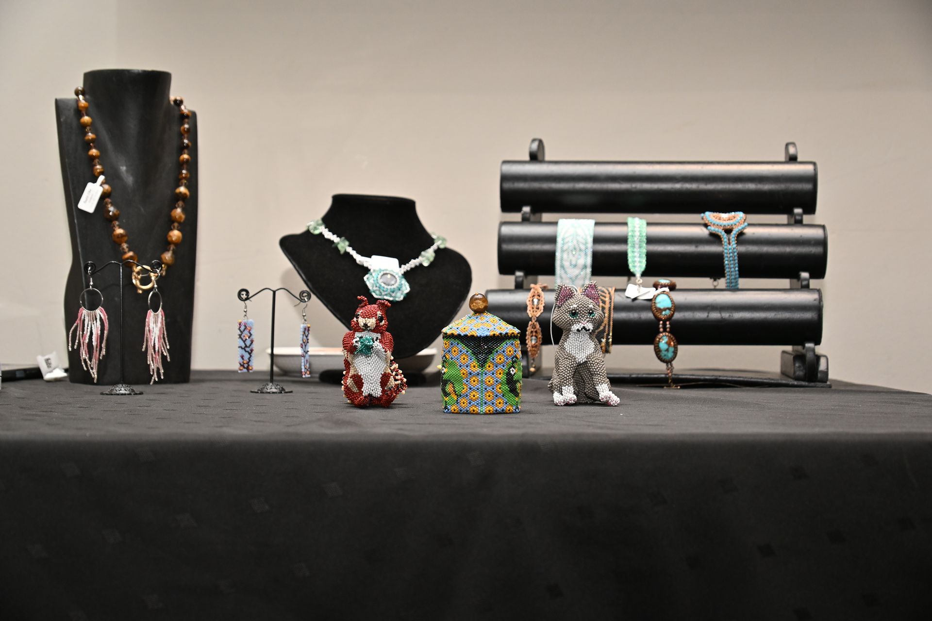 Jewelry display with beaded necklaces, bracelets, and figurines on black stands and a table
