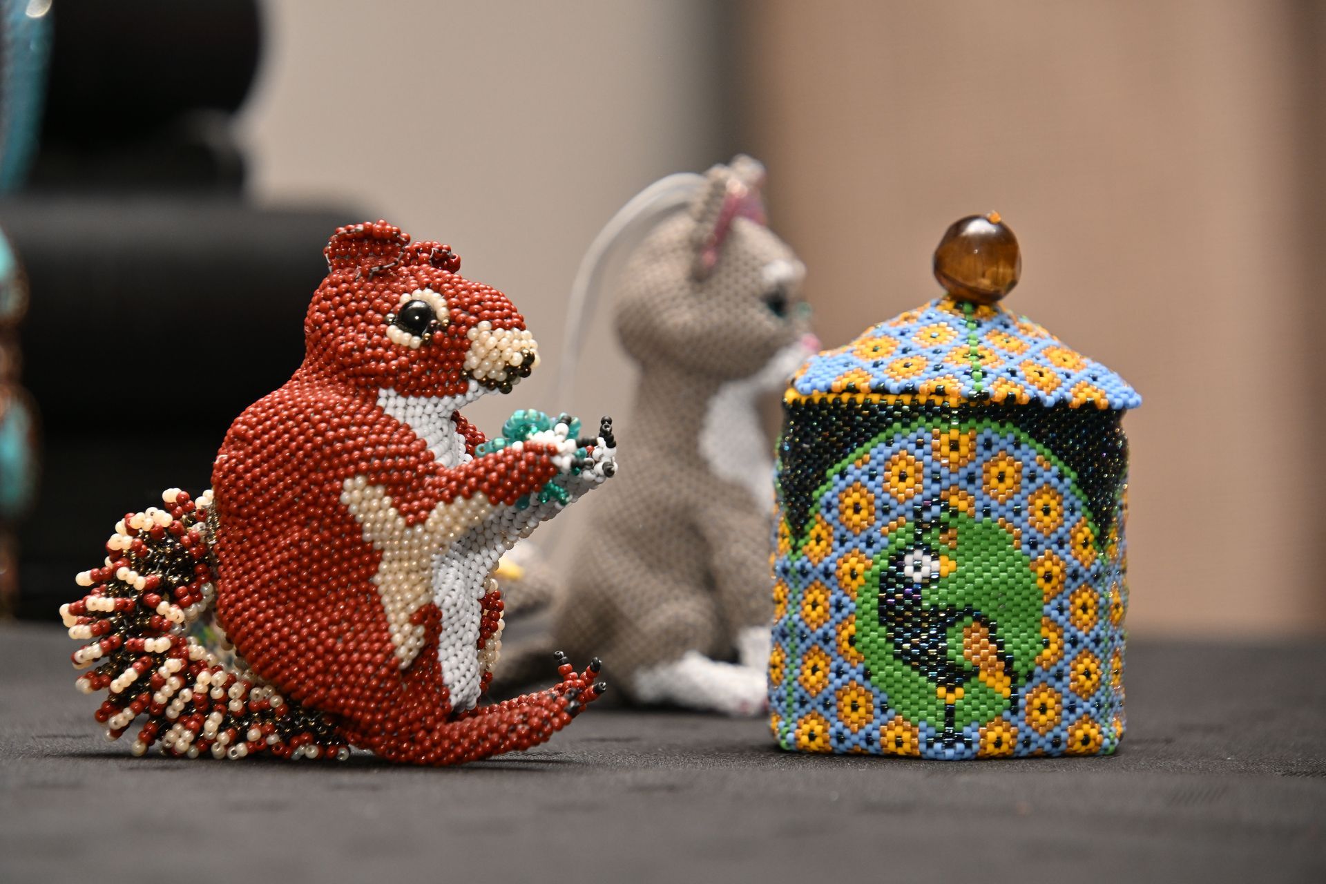 Colorful beaded squirrel figurine beside a gray animal and mosaic-patterned house on a table