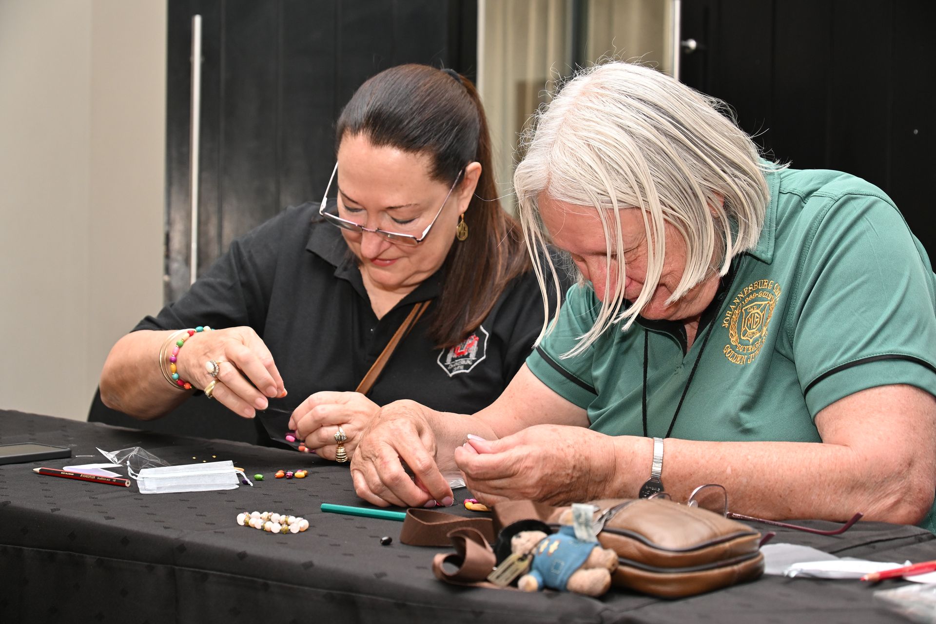 Two people seated at a table, carefully crafting small items with tools and materials spread out.