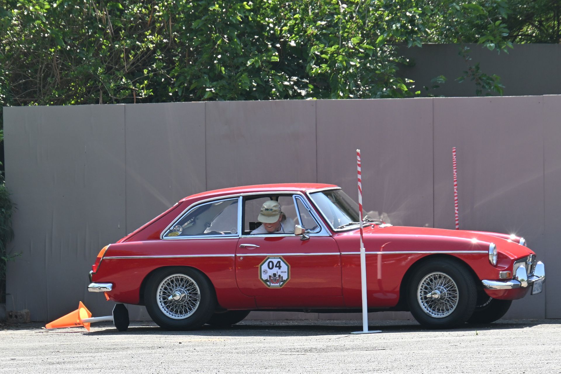 Red vintage car in a side-view parking test setup beside traffic cones and a gray barrier.